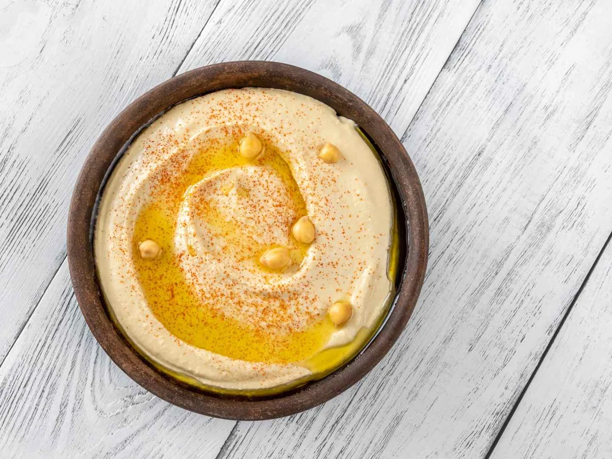 A small wooden bowl of hummus topped with oil and paprika