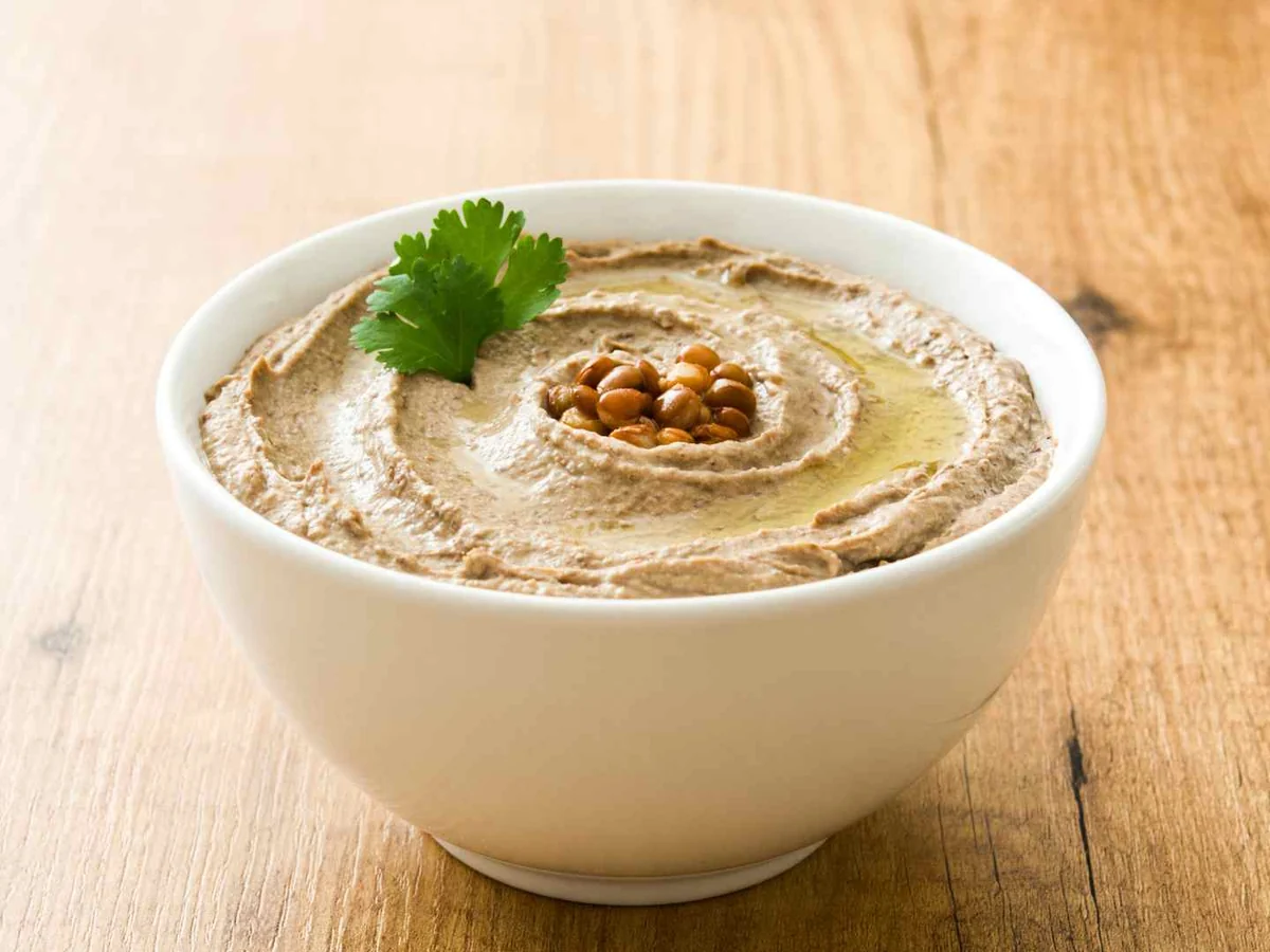 A white bowl of hummus garnished with chickpeas and cilantro