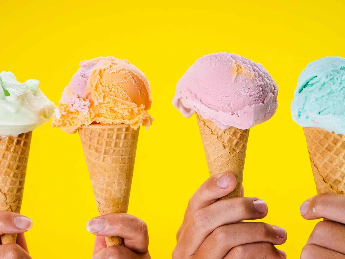Four hands holding colorful ice cream cones against a bright yellow background