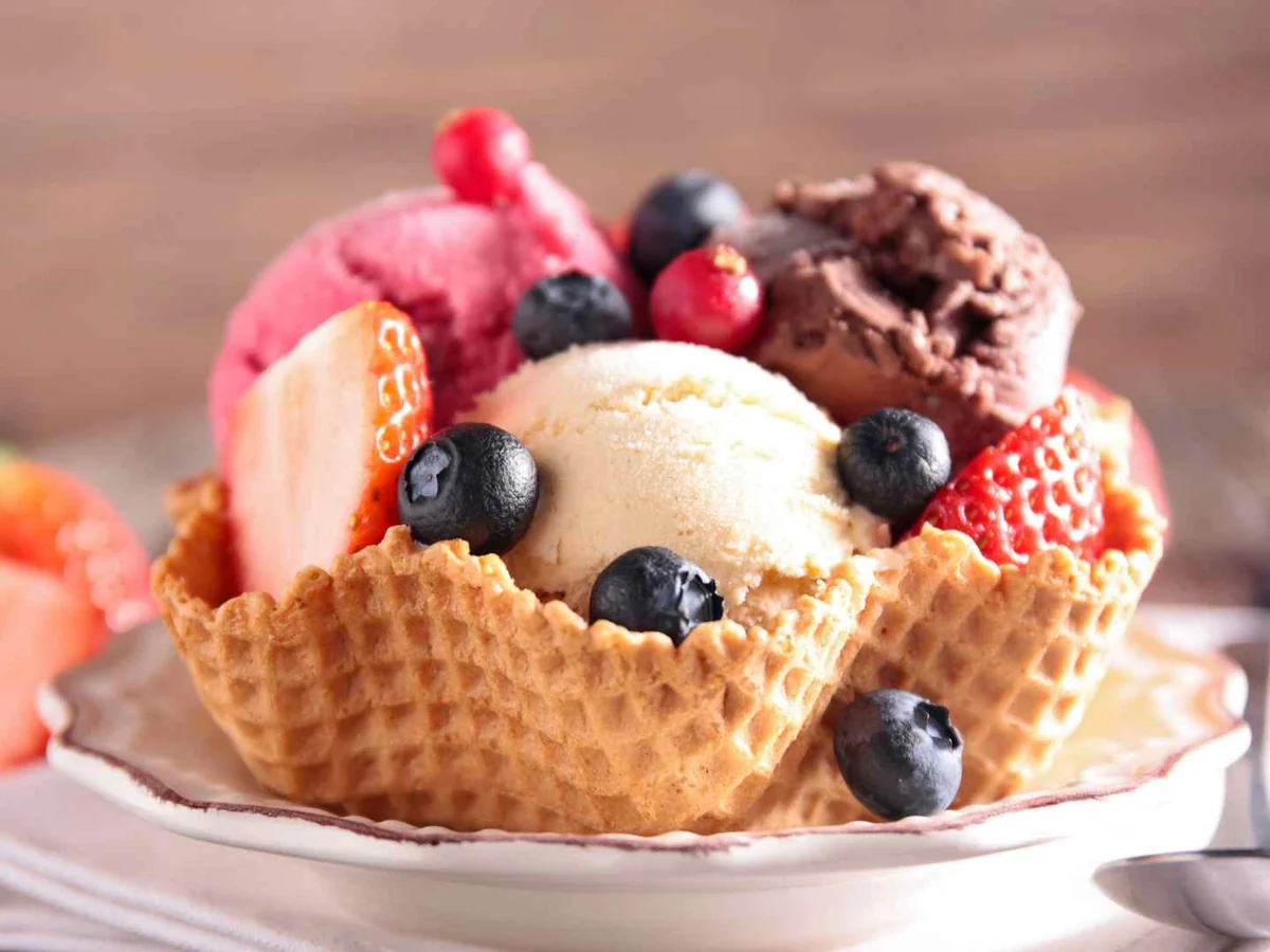 A waffle bowl filled with several ice cream flavors and fresh berries