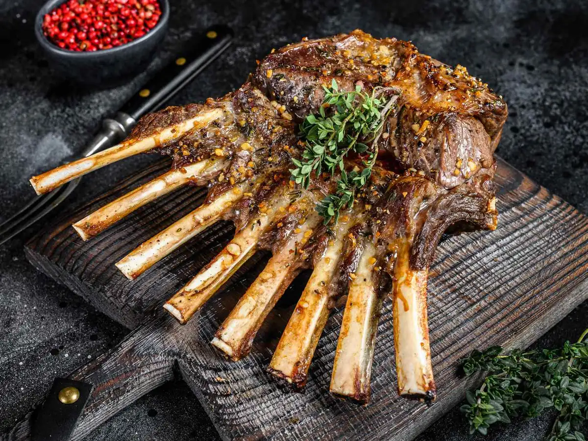 A cooked rack of lamb on a dark serving board