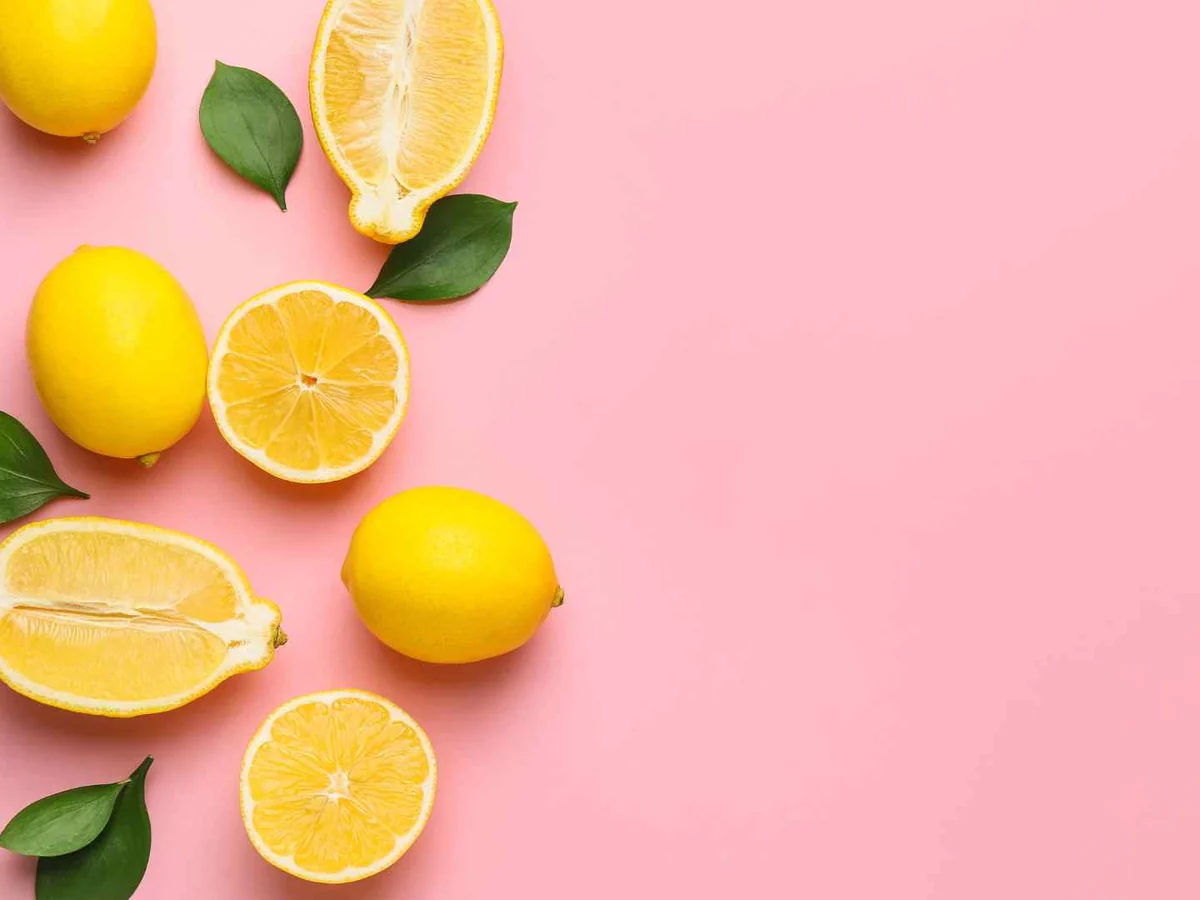 Whole and halved lemons arranged on a pink background