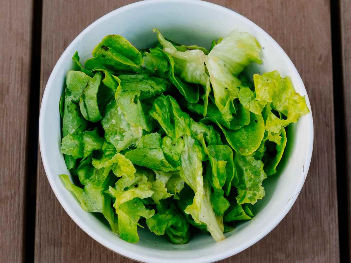 A white bowl of chopped green lettuce on a dark wooden table