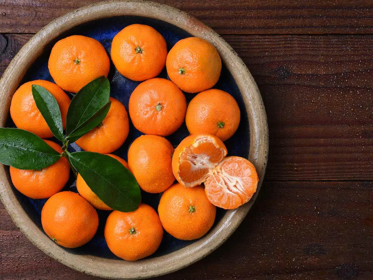 Whole mandarins with leaves in a dark bowl