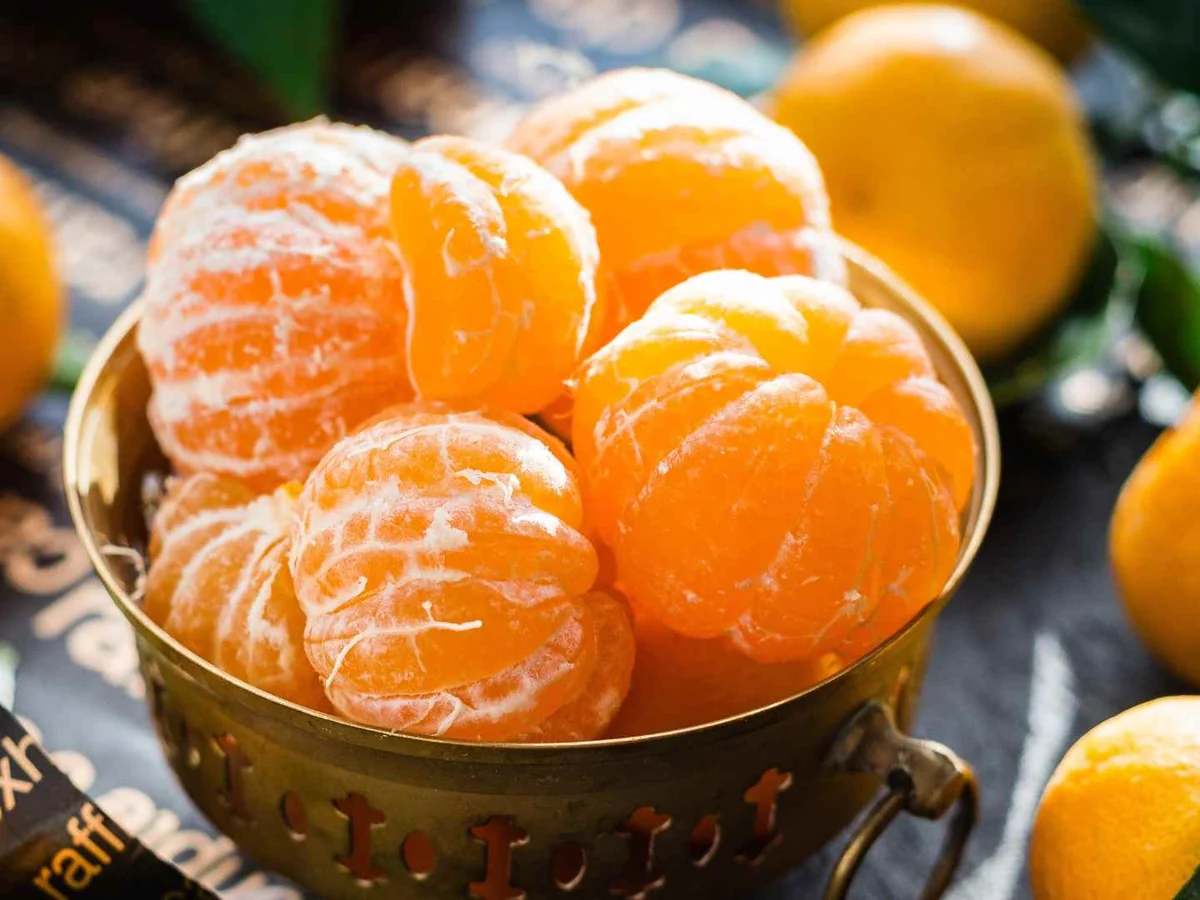 Peeled mandarins in a metal cup beside whole fruit