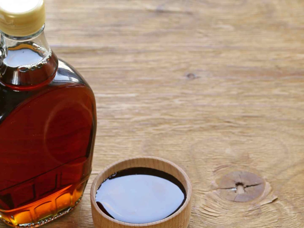 Amber maple syrup in a rounded bottle beside a small white dish.