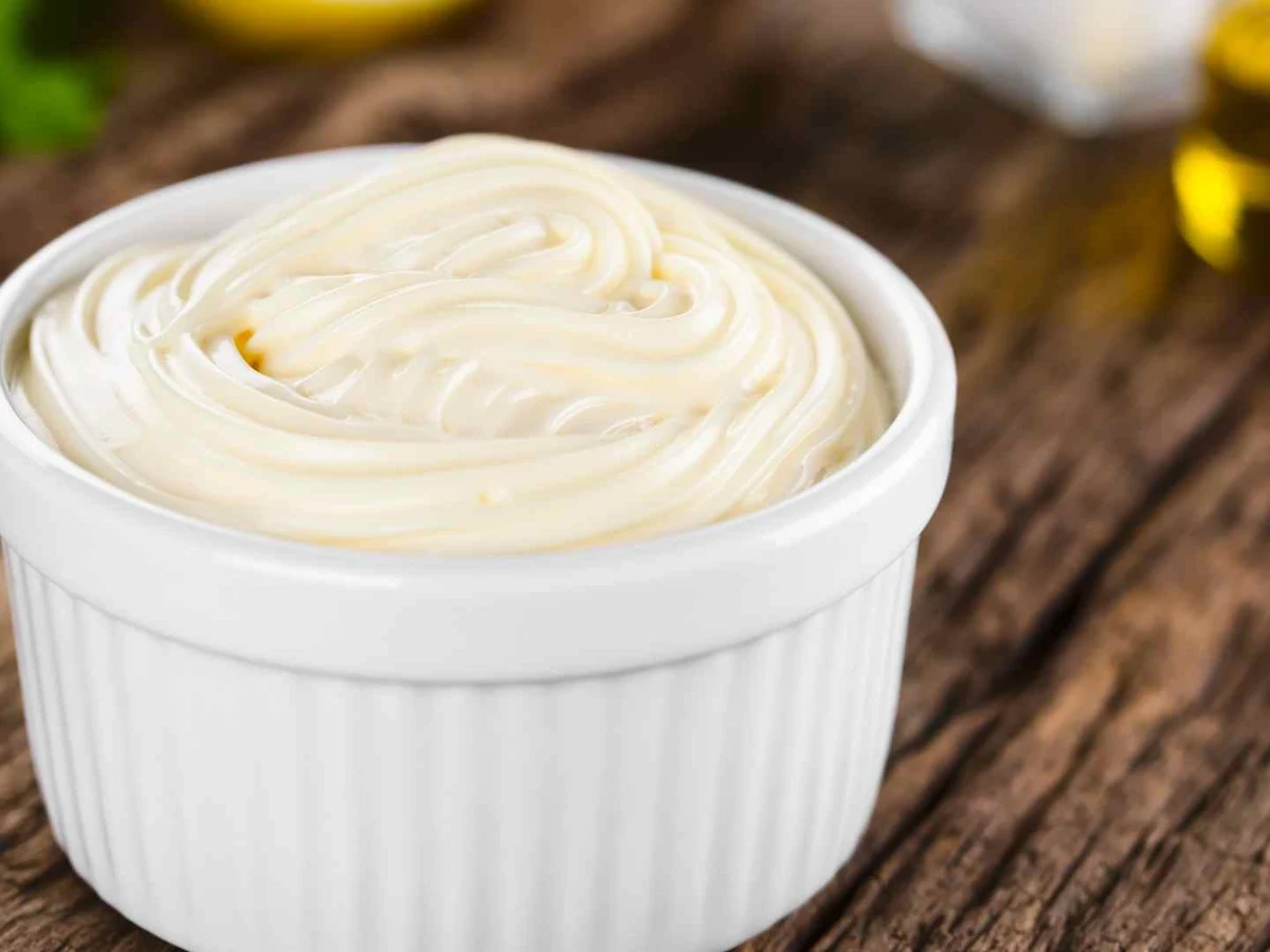 A small bowl of pale mayonnaise flecked with green herbs.