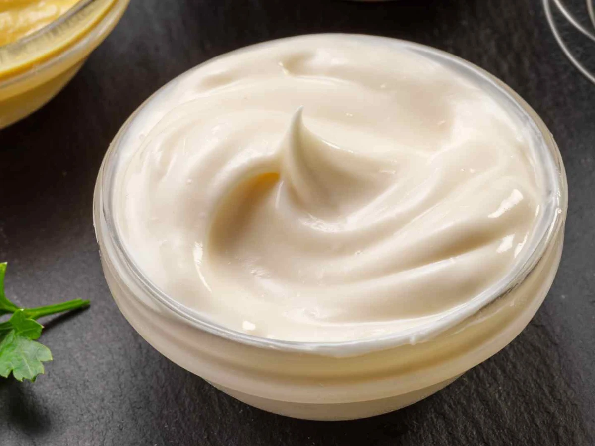 Smooth mayonnaise swirled in a white ramekin on a wooden table.