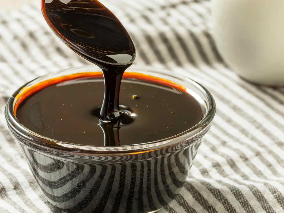 Dark molasses pouring from a spoon into a small bowl
