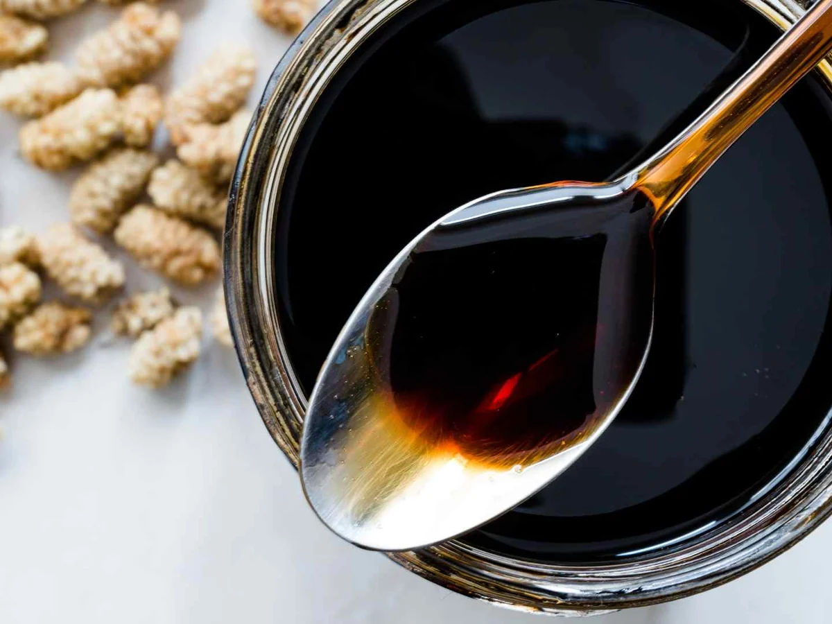 A bowl of dark molasses with a spoon and pale seeds behind it