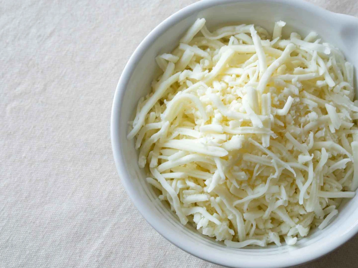 Creamy mayonnaise in a glass bowl beside parsley and lemon.