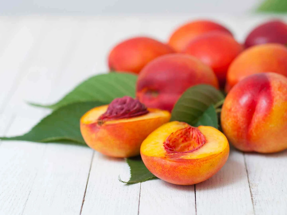 Whole and halved nectarines on a pale wooden table