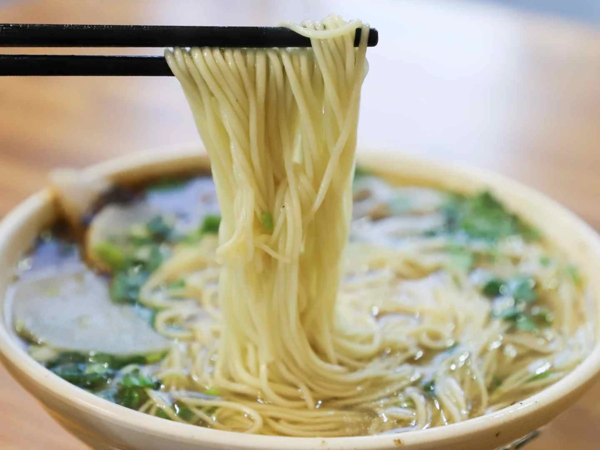 Shredded white mozzarella in a bowl with loose strands on cloth.