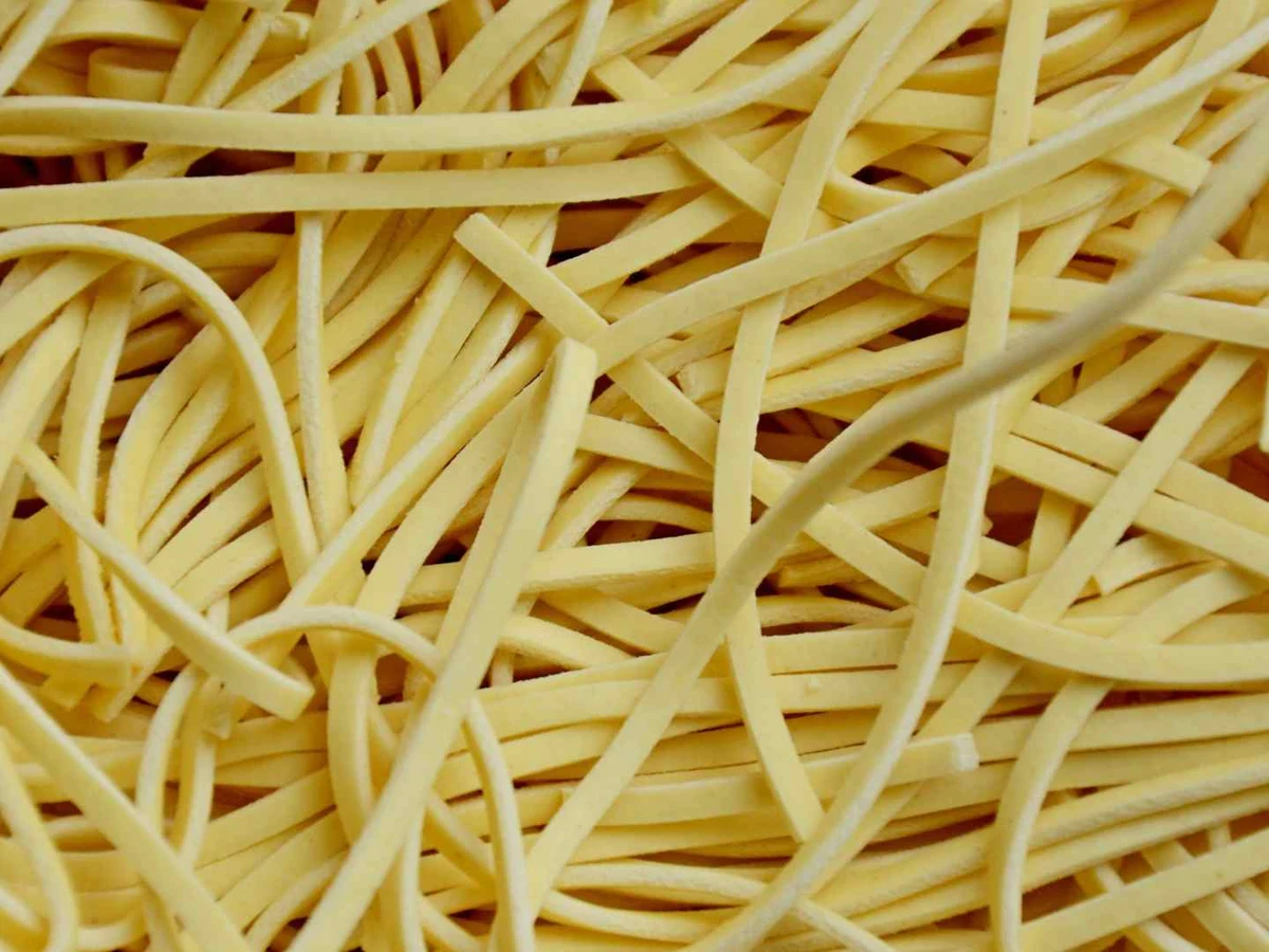 Curly noodles lifted from a cup with chopsticks.