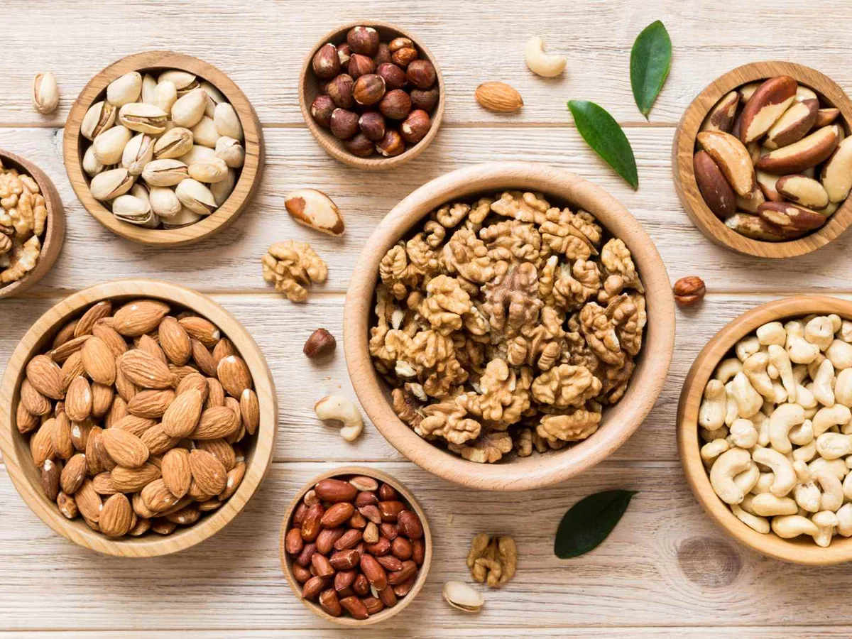 Several bowls containing different kinds of nuts on a pale wood table