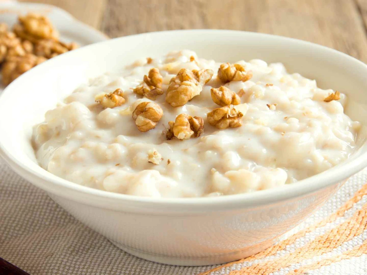 Creamy cooked oatmeal topped with walnut pieces in a white bowl.