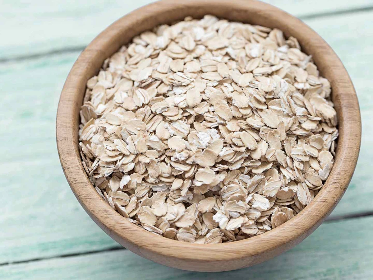 Rolled oats in a wooden bowl beside standing wheat stalks.