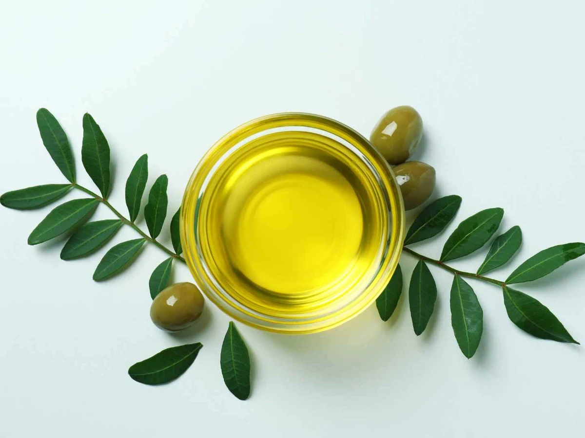 A glass bowl of olive oil viewed from above between olive branches.