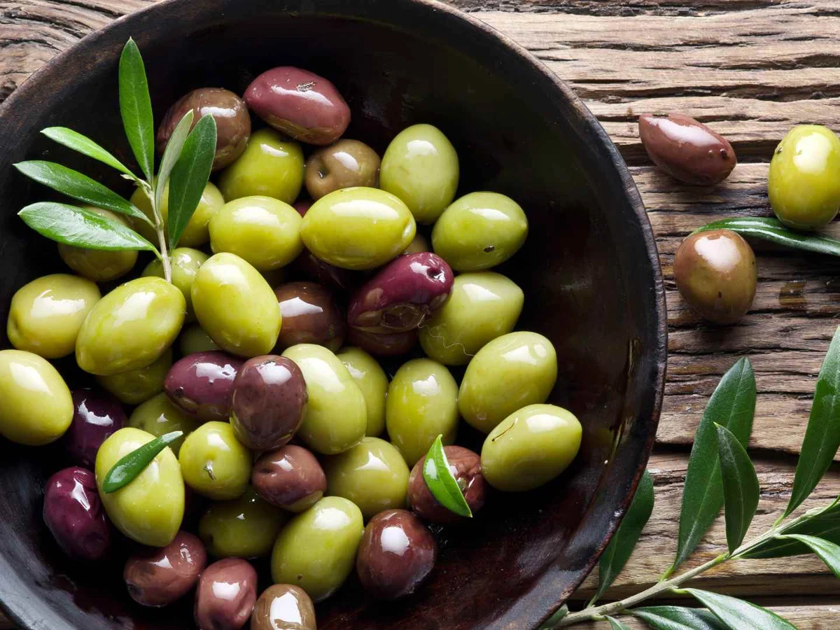 A dark bowl of green and purple olives on a rustic wooden table