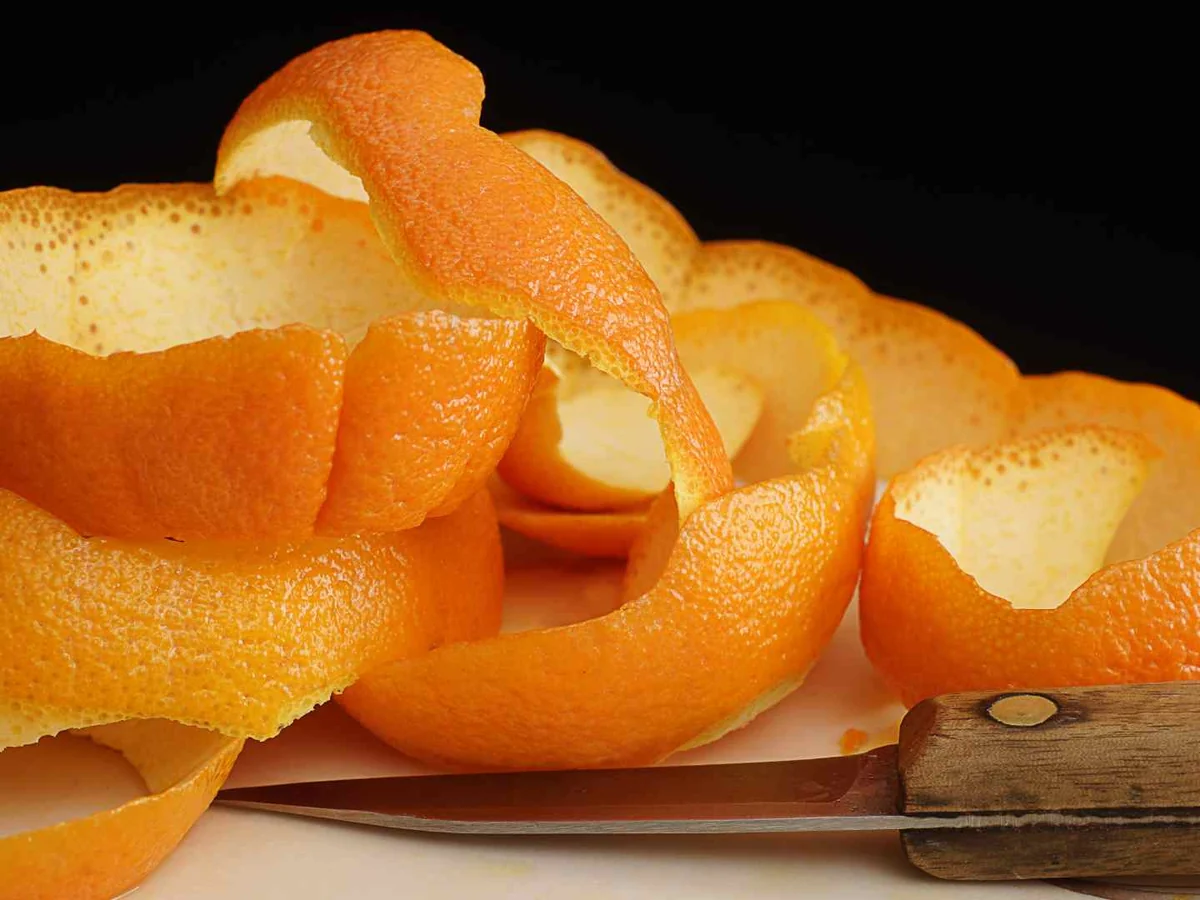 A long orange peel beside a knife on a black background