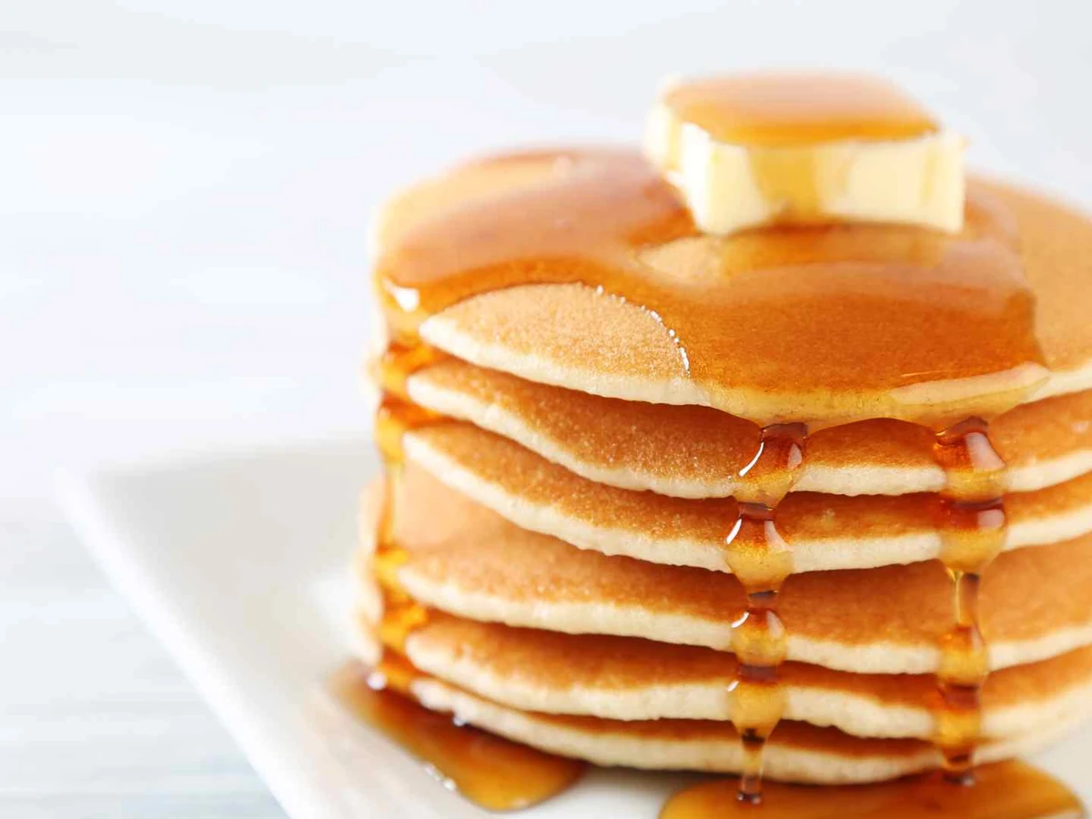 A stack of pancakes covered with syrup against a bright white background.