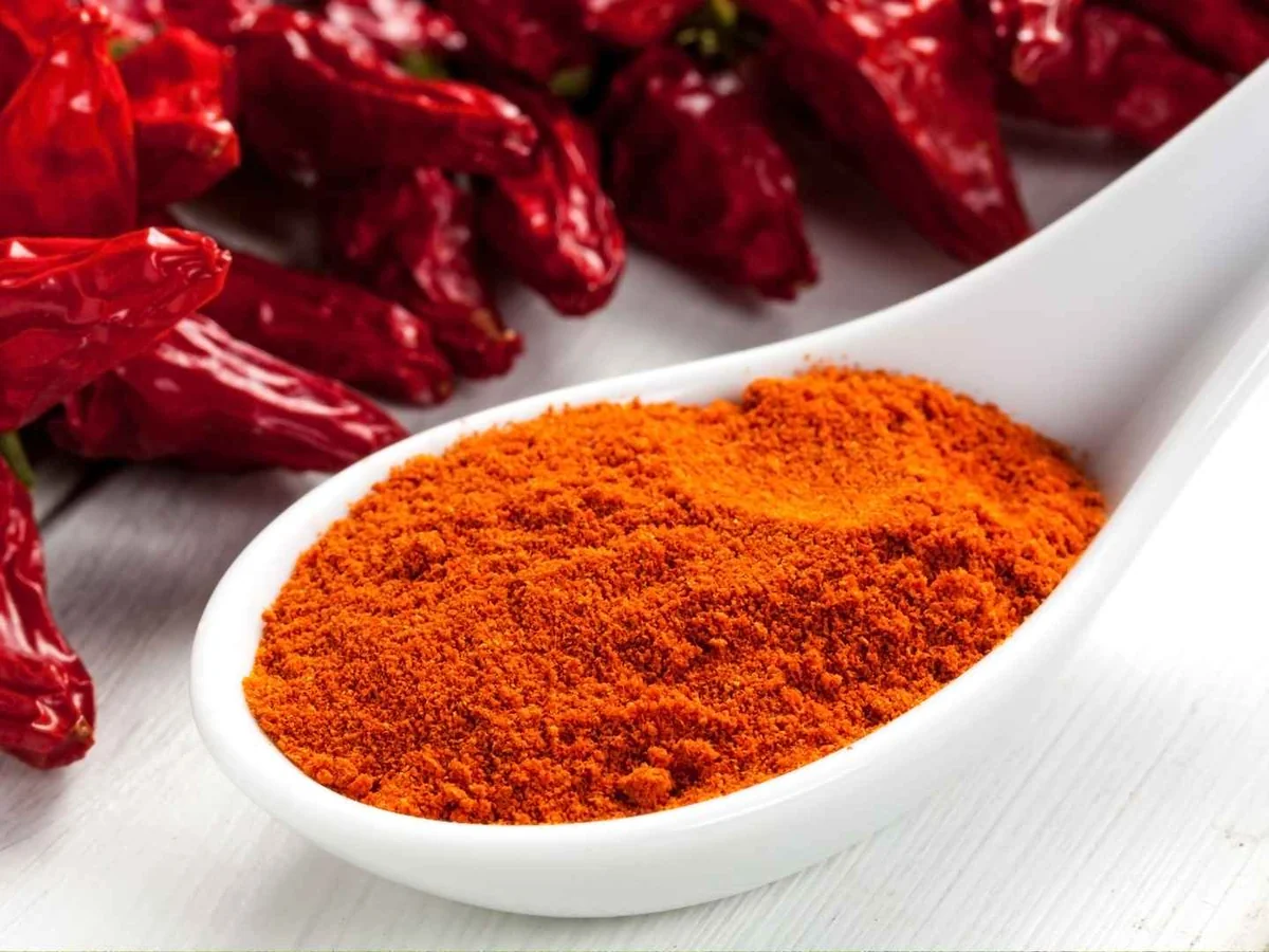 Red paprika powder in a white spoon beside dried peppers
