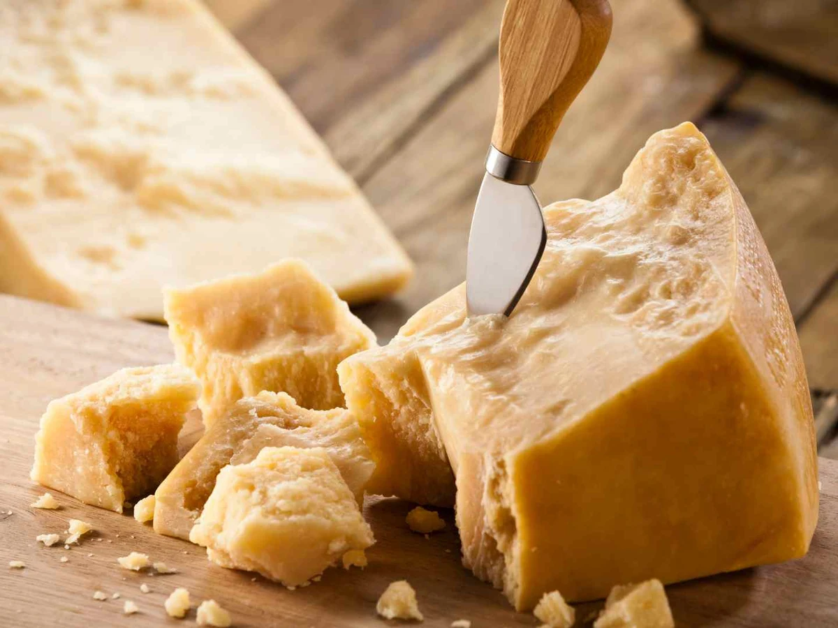 Finely grated Parmesan beside a large wedge on a wooden surface.