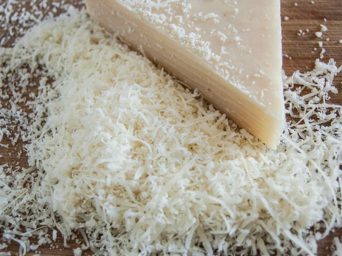 Hard Parmesan wedges being cut with a small cheese knife.