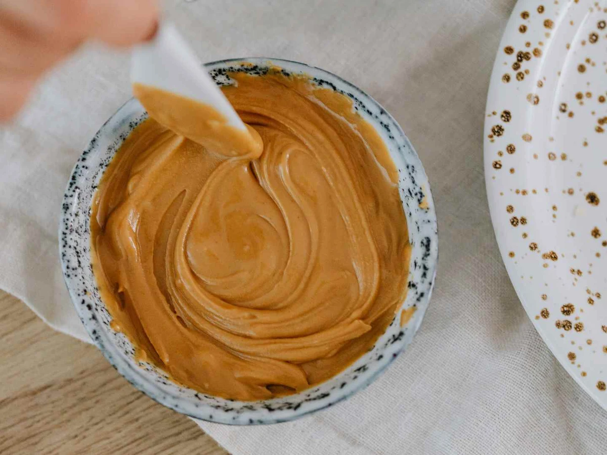 Creamy peanut butter in a ceramic bowl beside a spoon.