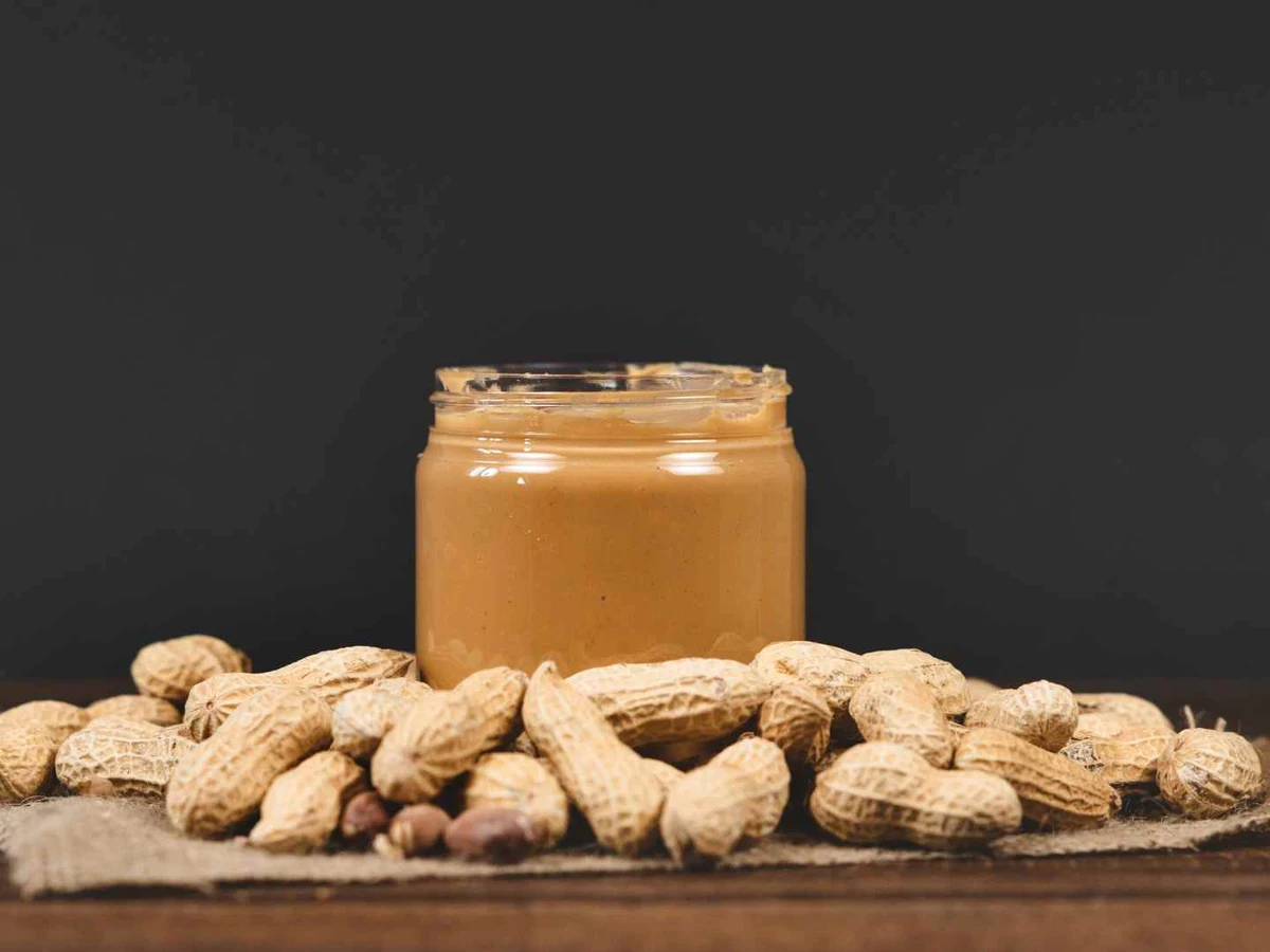 A jar of peanut butter surrounded by whole peanuts against a dark background.