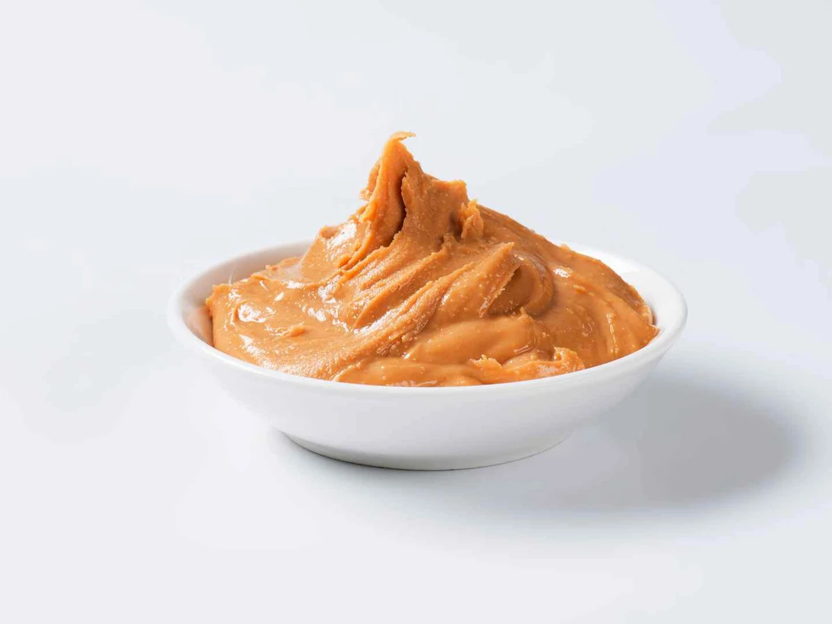 A small white dish of creamy peanut butter on a pale background.