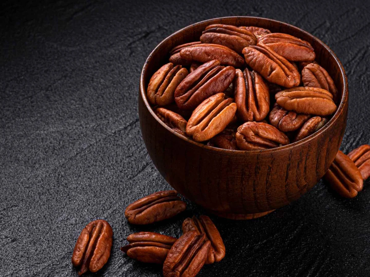 Pecan halves filling a wooden scoop and scattered on a blue wooden surface.