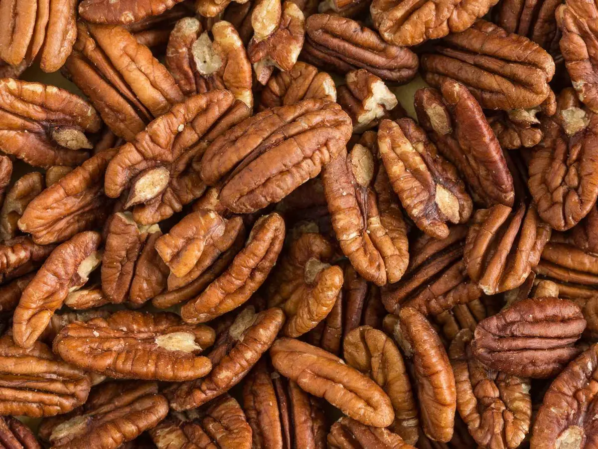 Pecan halves in a dark wooden bowl on a black surface.