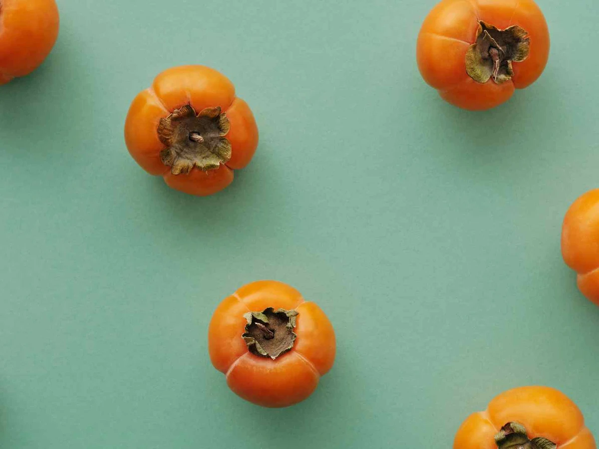Four whole orange persimmons in a shallow woven basket.