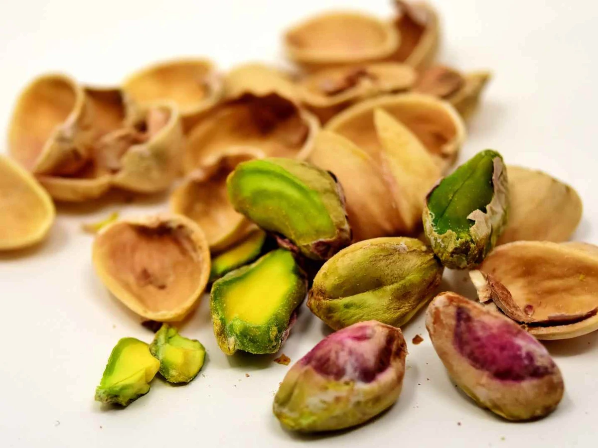 Cracked pistachio shells and several kernels scattered on a white surface.