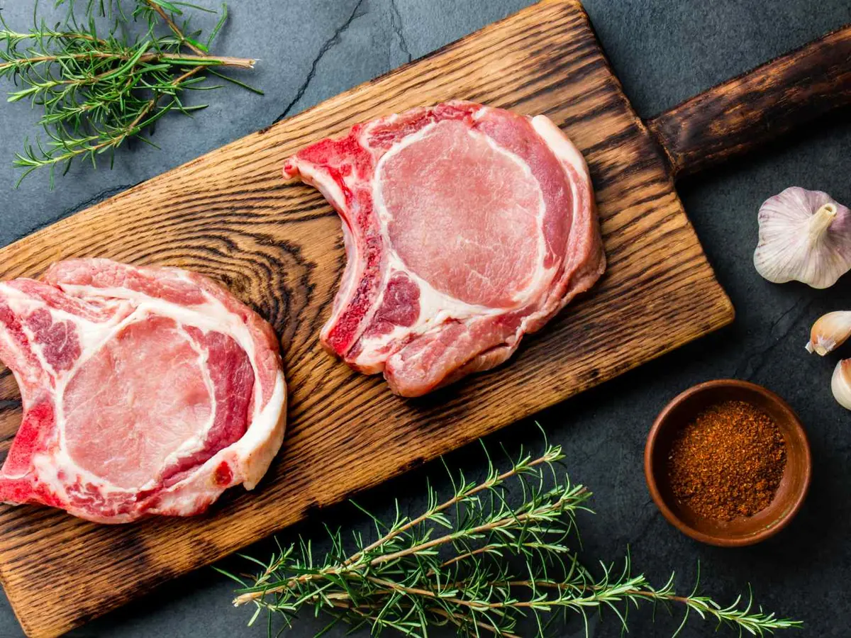Two raw bone-in pork chops on a wooden cutting board