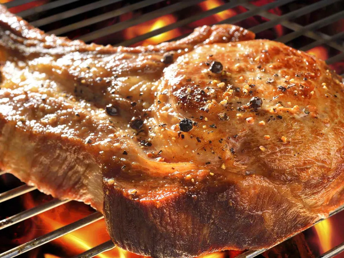 A bone-in pork chop cooking on a grill