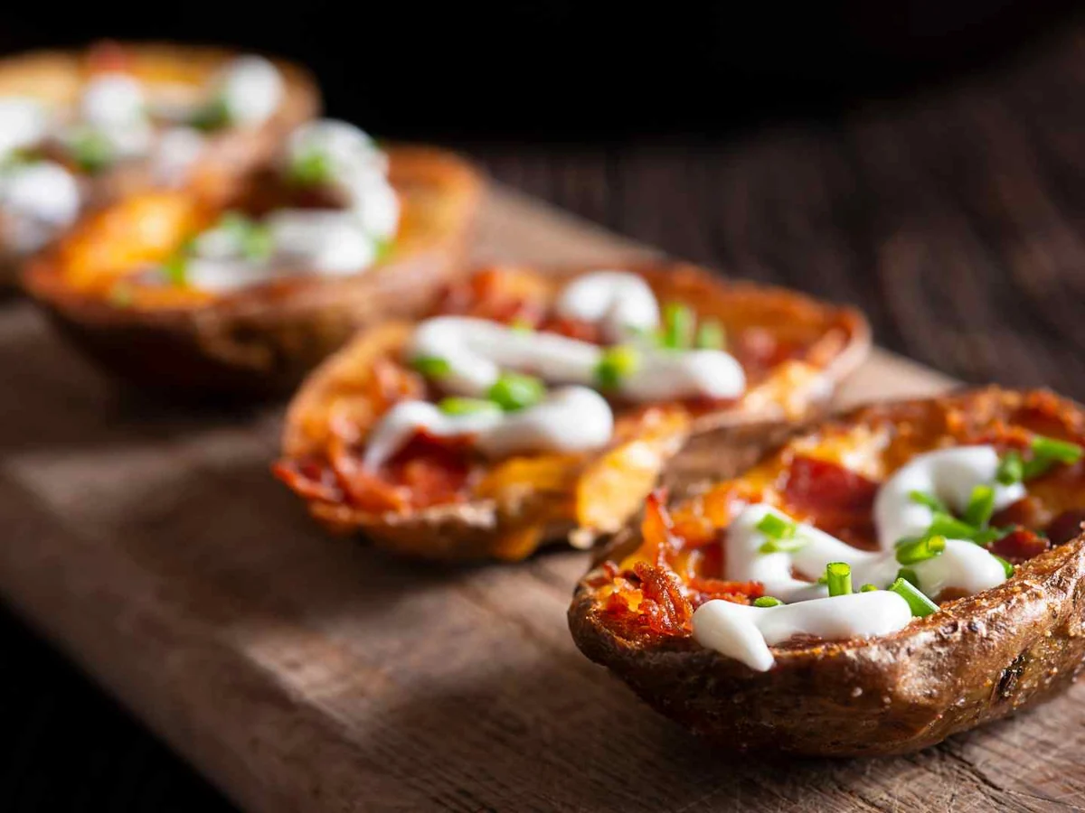 Loaded potato skins topped with cheese and sour cream on a dark board