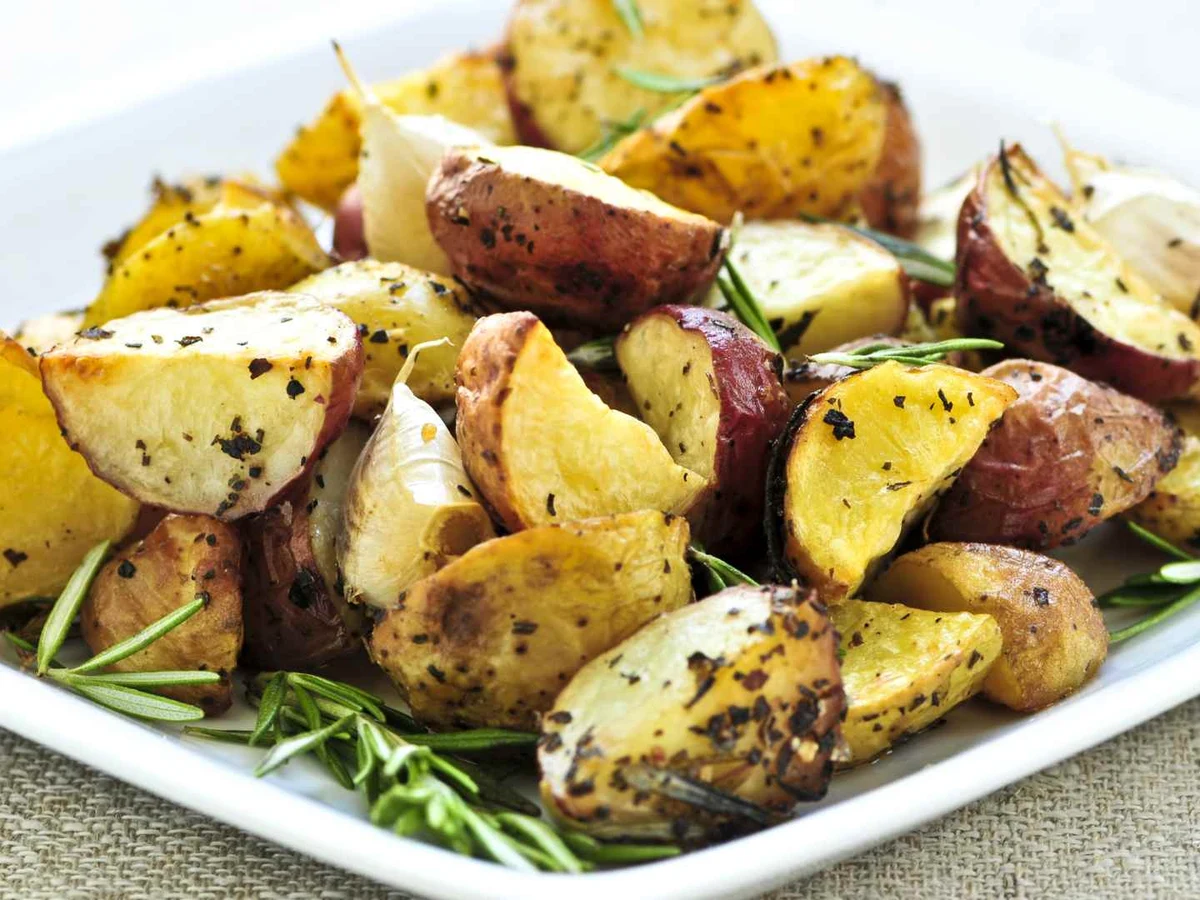 Roasted potato wedges with herbs arranged on a white rectangular plate.