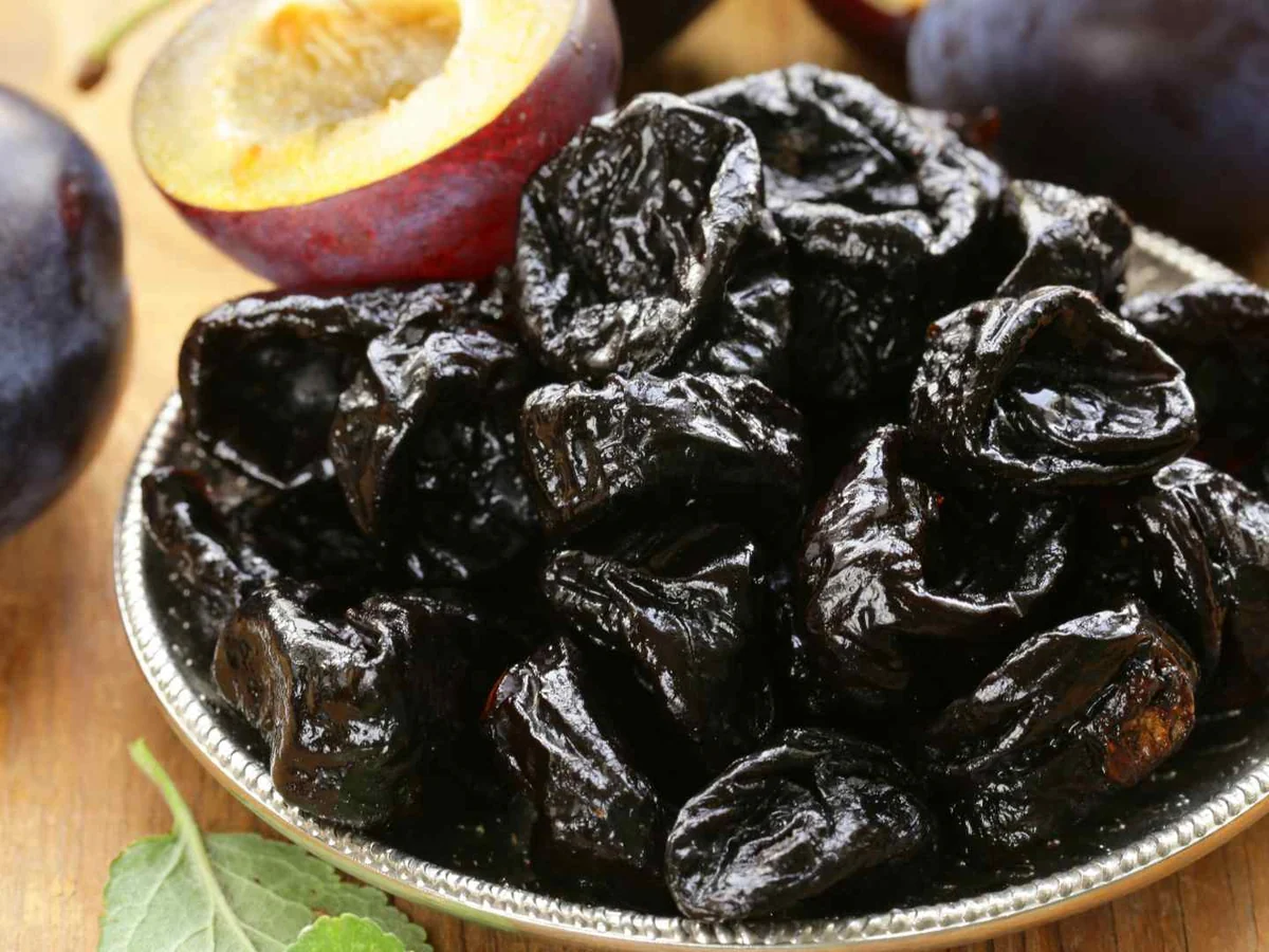 A bowl of glossy prunes surrounded by fresh plums