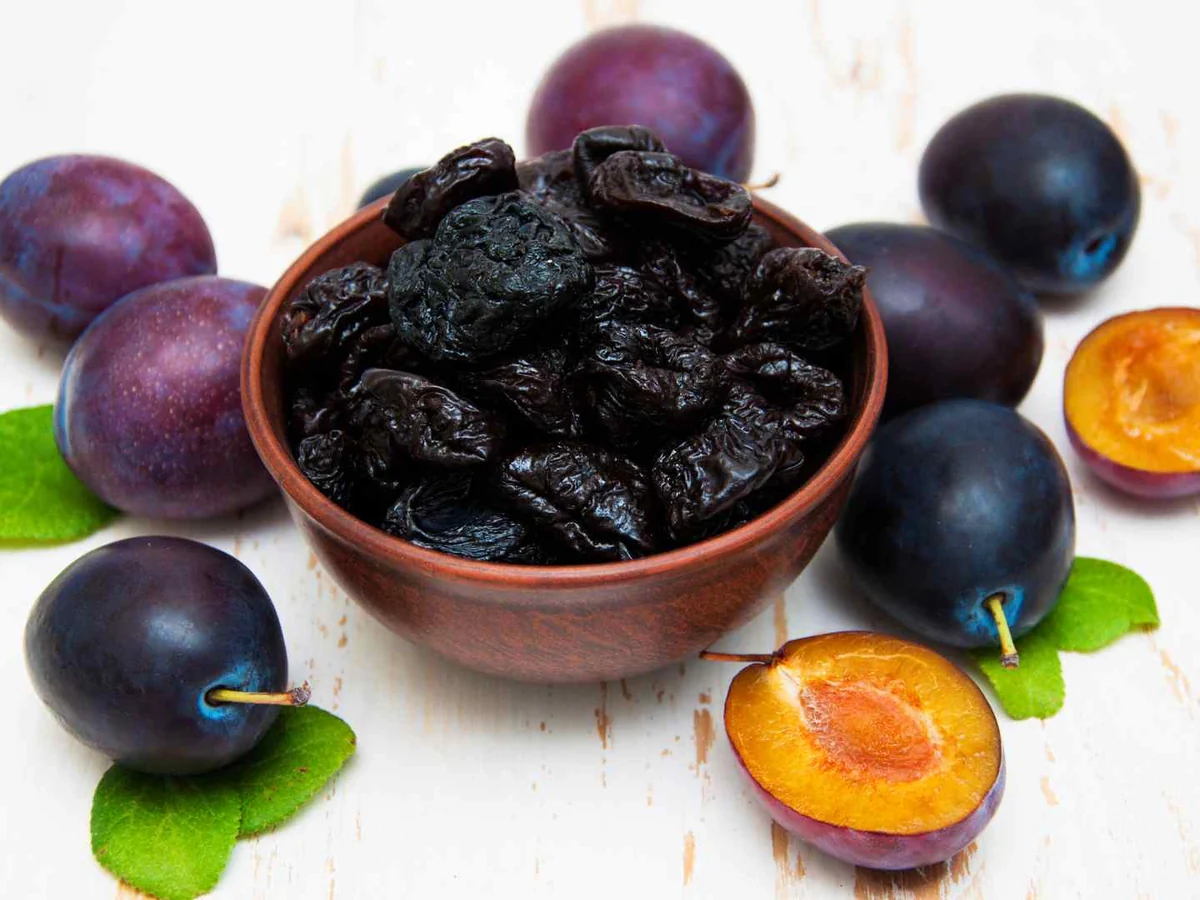 A bowl of prunes with fresh plums and green leaves