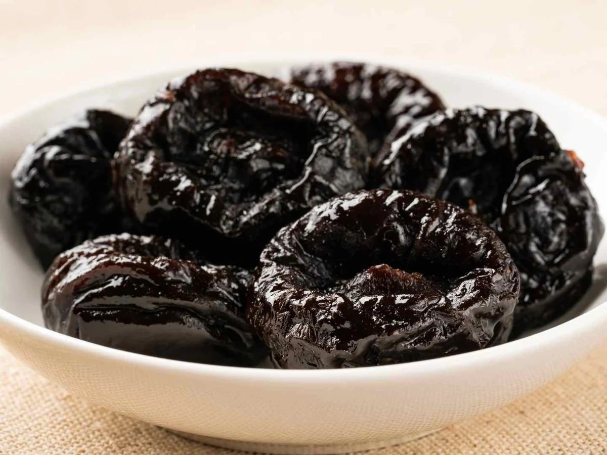 A white bowl filled with glossy prunes