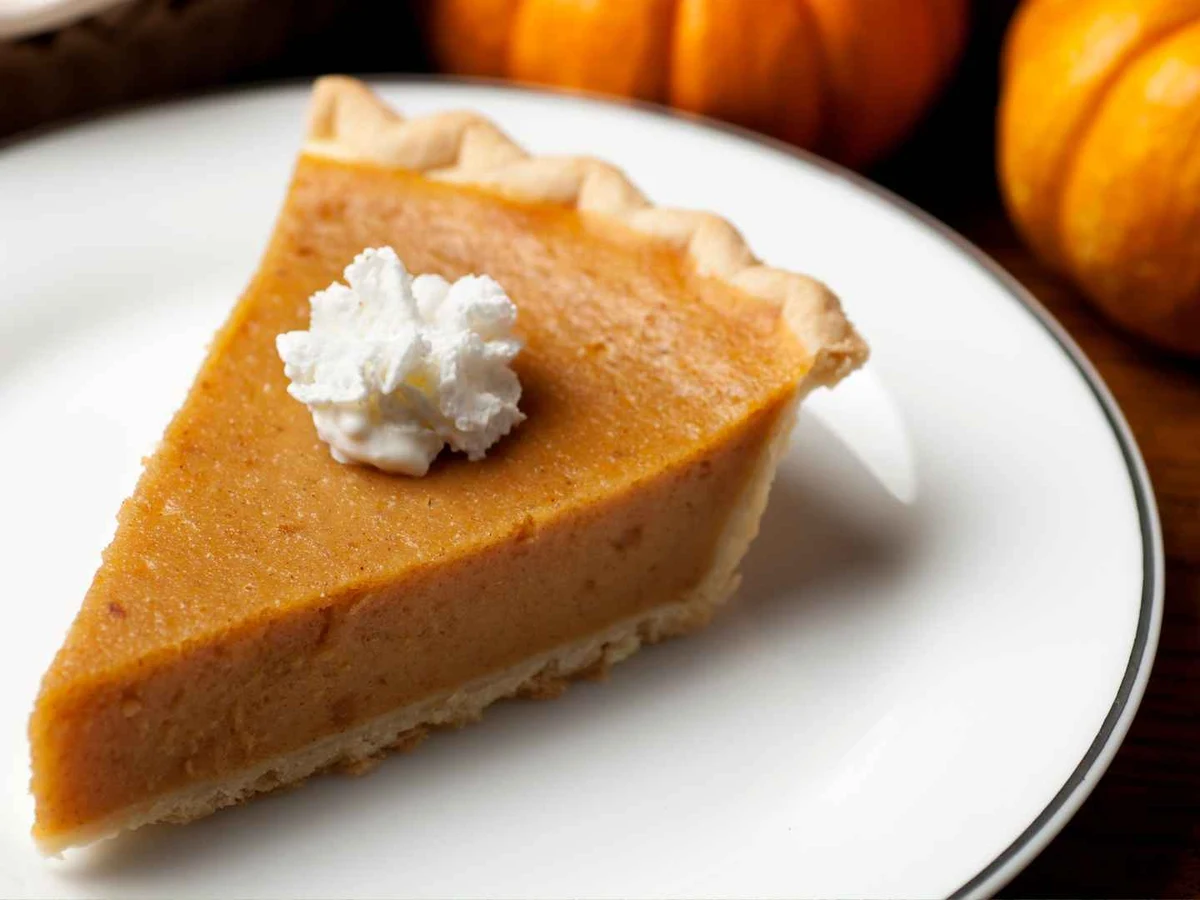 A slice of pumpkin pie topped with whipped cream on a plate.