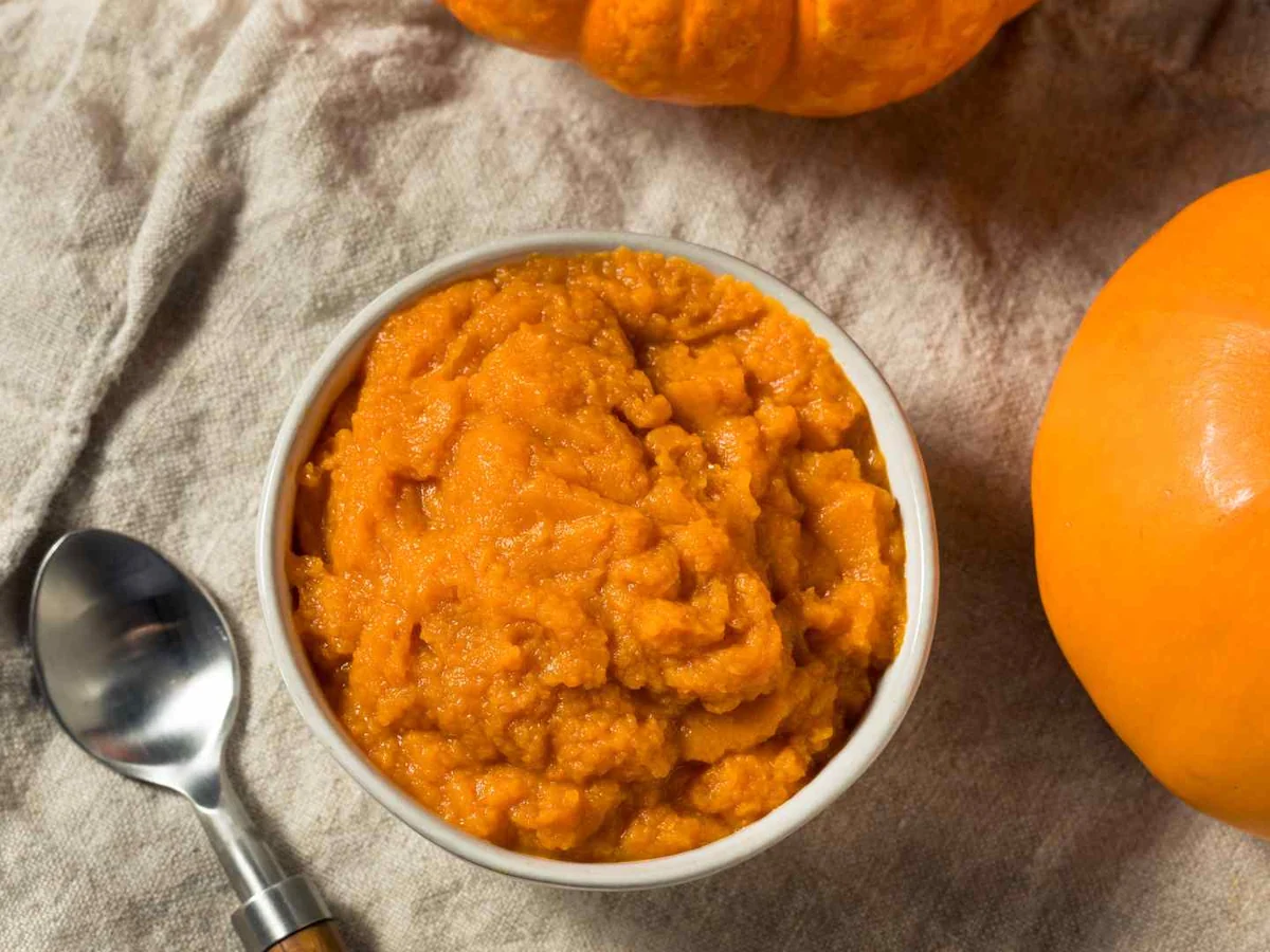 A bowl of pumpkin puree beside whole and cut pumpkins