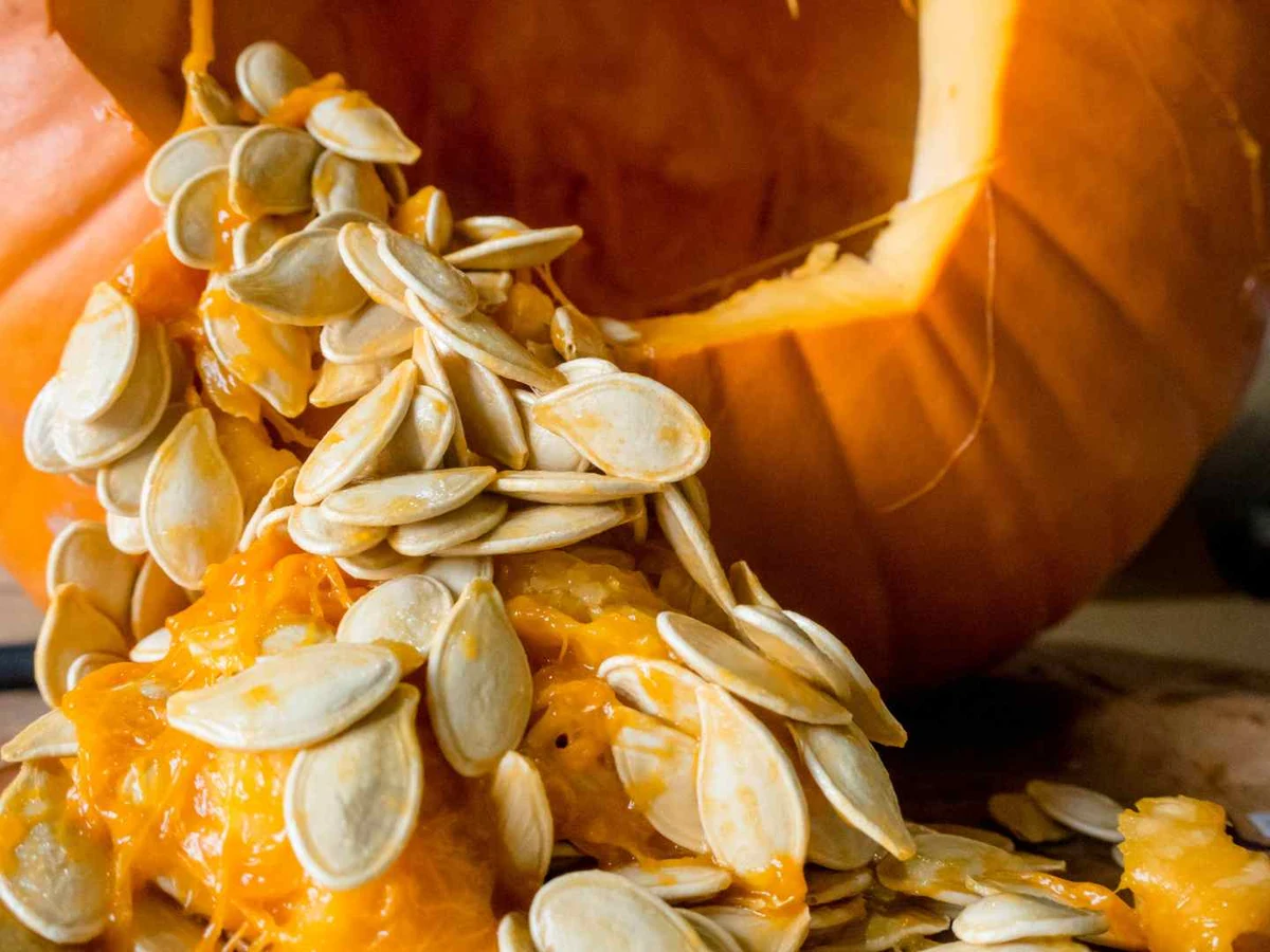 Green hulled pumpkin seeds in a wooden bowl beside a small pumpkin.
