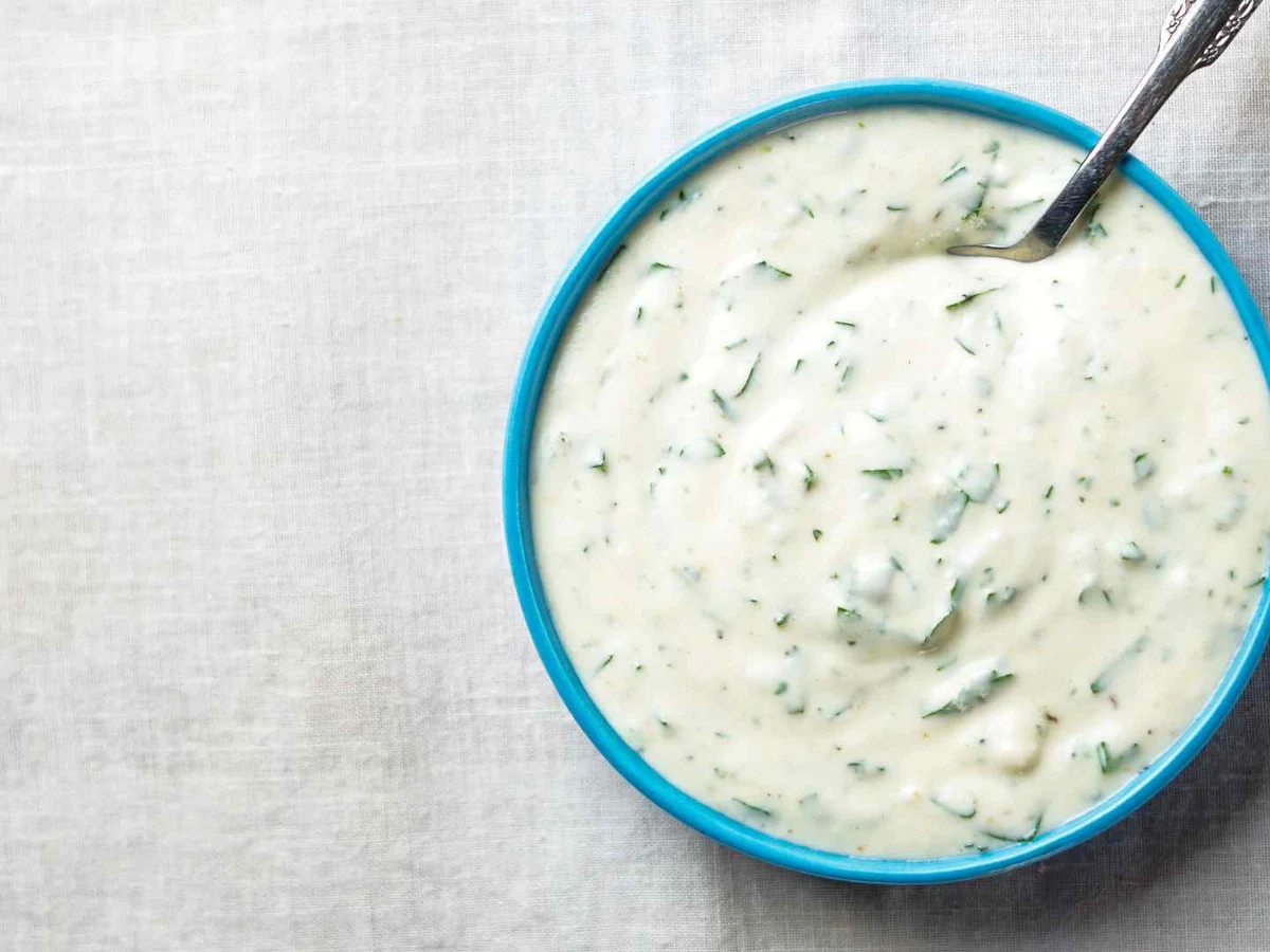 A white ramekin of creamy ranch dressing on a pale background.