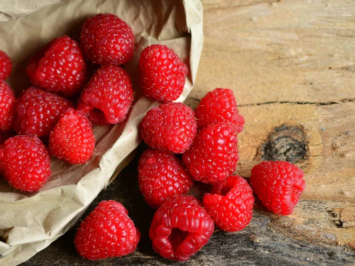 Fresh raspberries spilling from a paper bag onto a wooden table