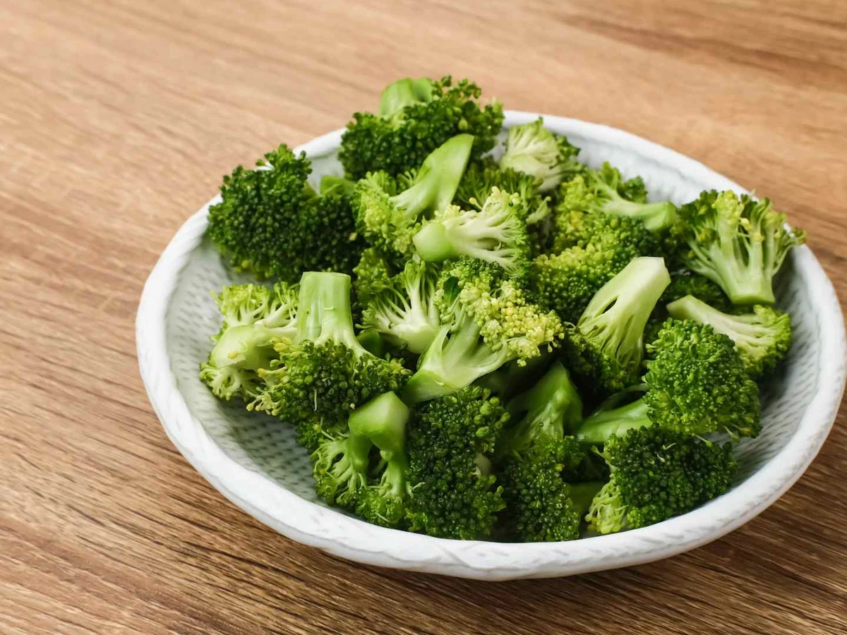 Raw broccoli florets in a brown bowl on a dark surface.