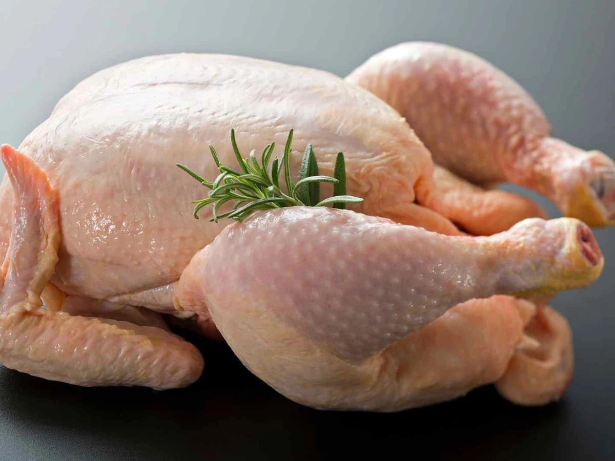 A whole plucked raw chicken resting on a plain gray surface.