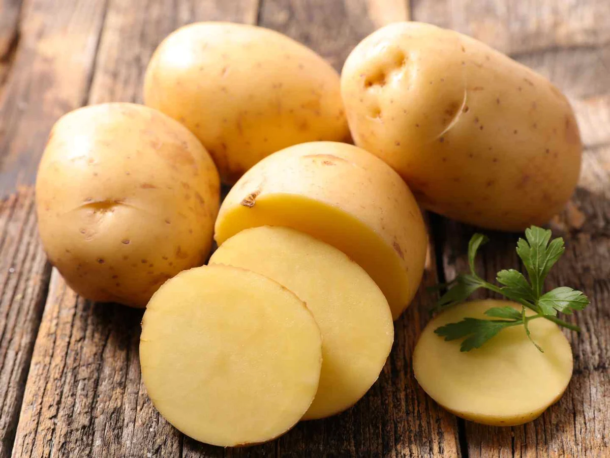 Whole and sliced raw yellow potatoes on a wooden table